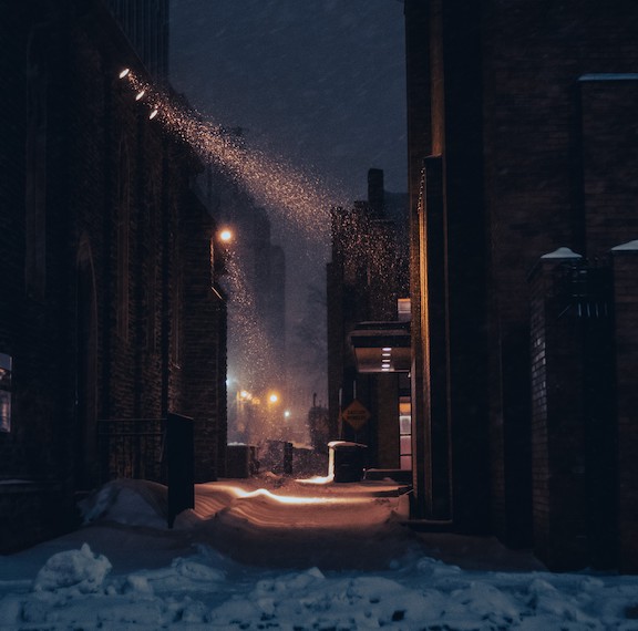 Alley way between two buildings. At night in the snow with some street lights lighting the road