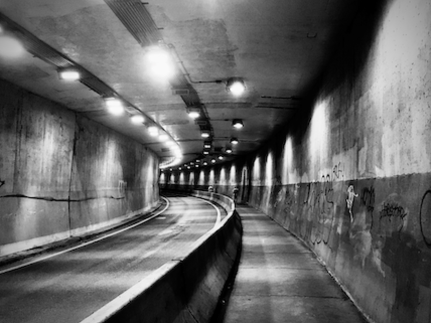 Black and white image of a curved tunnel with lights lighting up the tunnel
