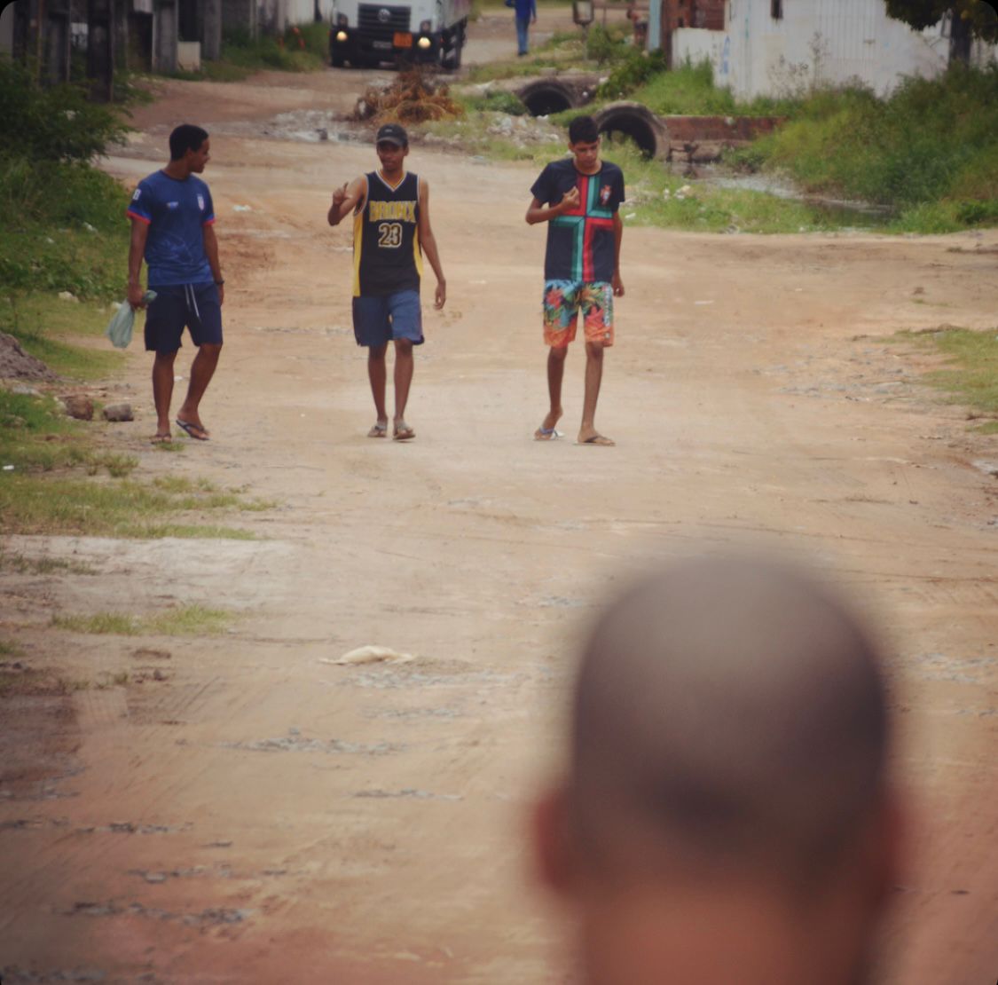 Photo of 3 boys talking to each other and walking on a dirt road