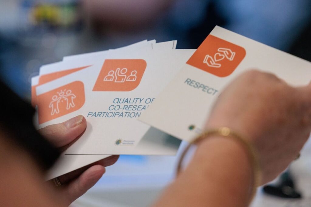 Person holding a pile of photovoice training cards; one says "Quality of co-research participation" and another that says "Respect"